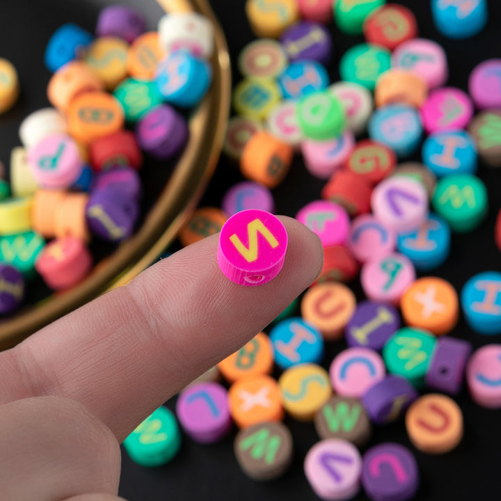 Close-up of colorful alphabet beads from Arts And More Bracelet Kit held on fingertip