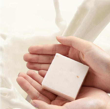 Hands holding a white square bar of Jasmine Rice Soap with creamy milk splash background