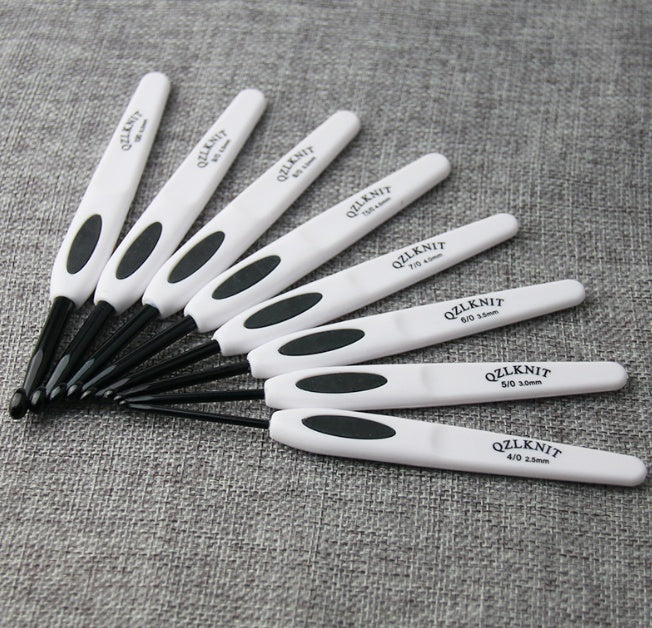 Set of aluminum crochet hooks with white ergonomic handles by Arts And More on gray fabric background