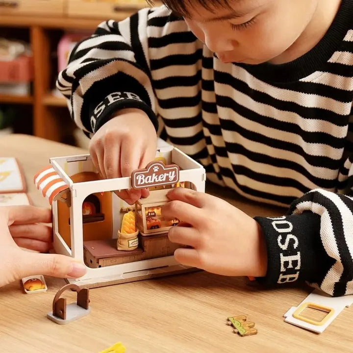 Child assembling the Rolife Food Box Shop DIY Miniature Kit with bakery accessories and details