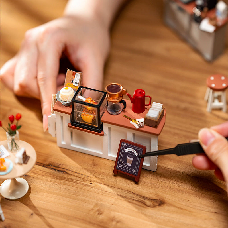 Person assembling a Cafe Miniature House Kit with detailed furniture and decorative items