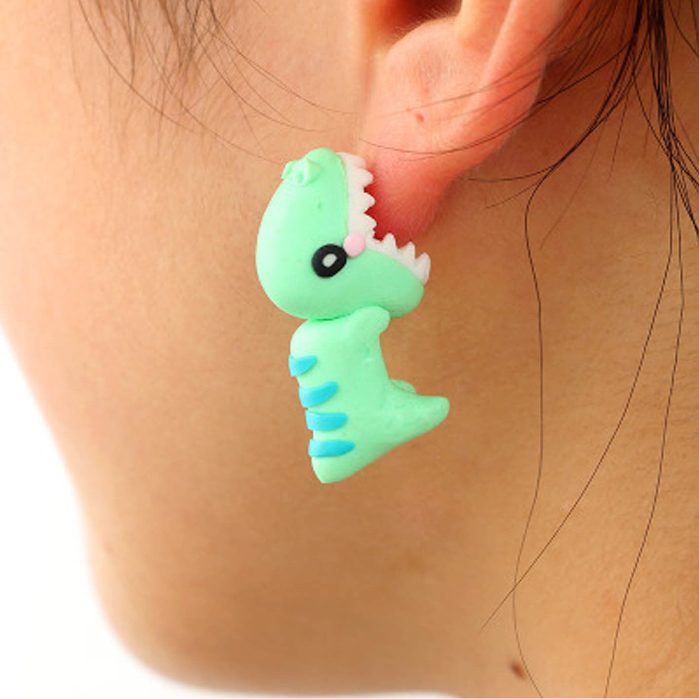 Green clay dinosaur shaped Clay Animal Earrings worn on ear, handmade from Arts And More
