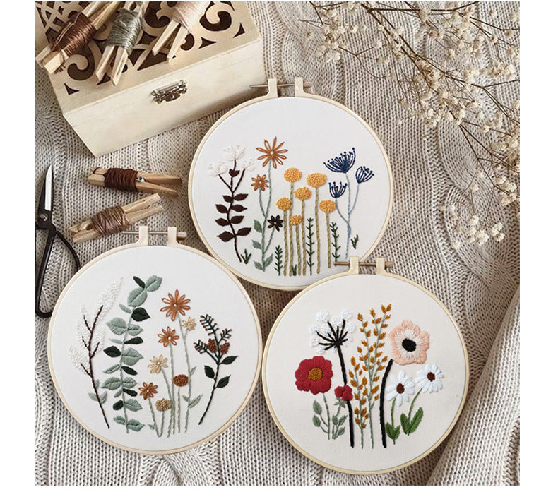 Three framed floral designs from the Dainty Stems Embroidery Kit displayed on a cozy background