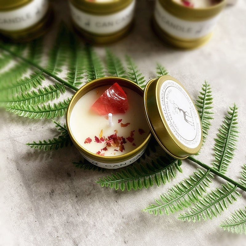 Gold Tin Box Scented Candle with Natural Ingredients and Floral Accents on a Green Leaf Background