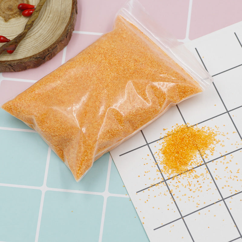 Arts And More Kids DIY Kits Magic Sand in orange color in a clear plastic bag with some spilled on a grid background