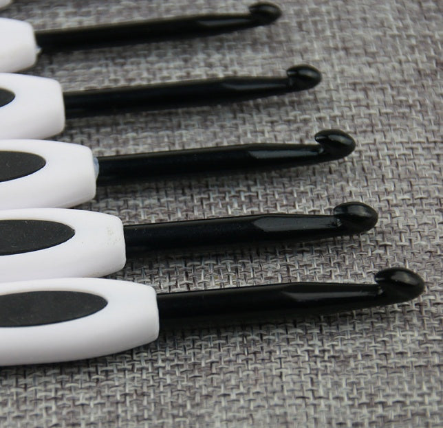 Arts And More crochet kit featuring black aluminum crochet hooks with white handles on gray fabric background