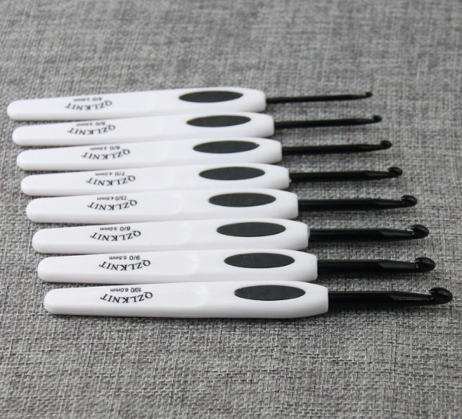 Arts And More aluminum crochet hooks set with white and black ergonomic handles on gray fabric