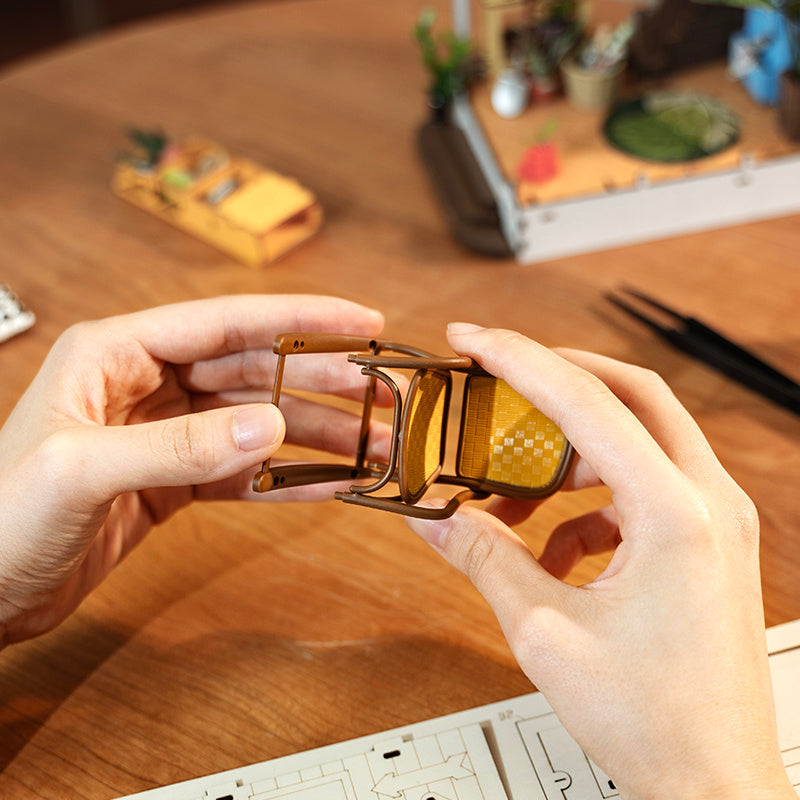 Close-up of hands assembling the Rolife Garden House Book Nook Kit chair with wooden details