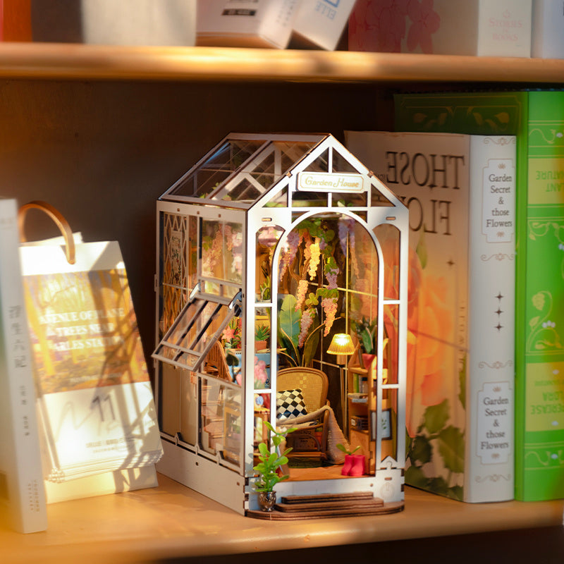 Rolife Garden House Book Nook Kit displayed on a shelf with colorful plants and cozy decor