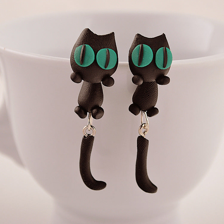 Soft Clay Earrings shaped like black cats with green eyes hanging on a white cup