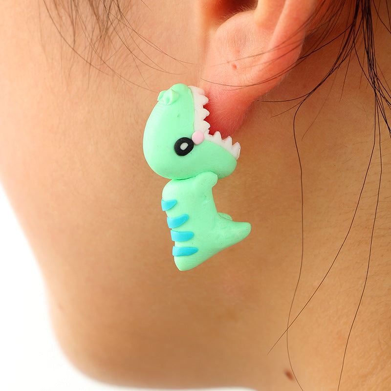 Green dinosaur-shaped soft clay earrings worn on ear from Arts And More decorations collection