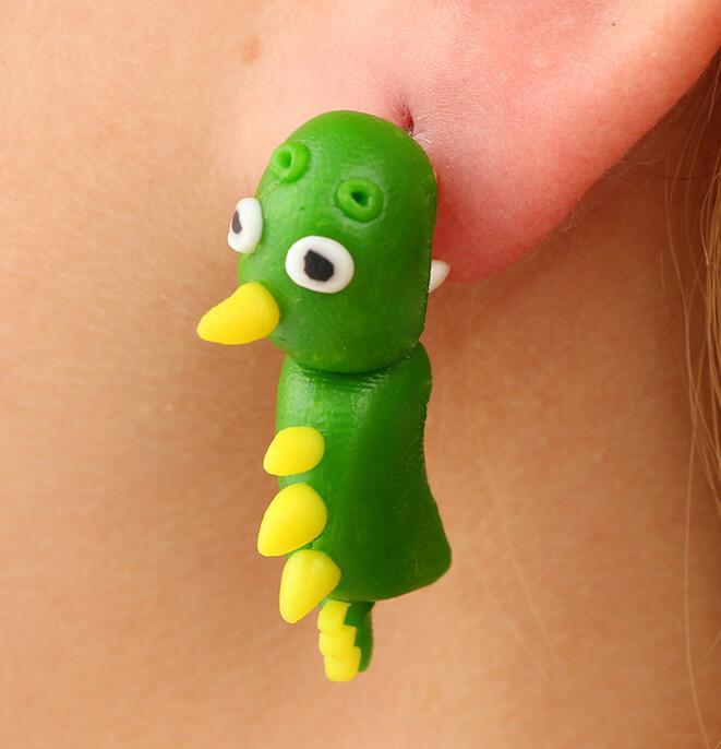 Green dinosaur soft clay earrings with yellow spikes worn on ear by Arts And More